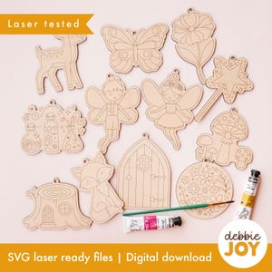May include: A collection of laser-cut wooden fairy-themed ornaments, including a deer, butterfly, fairy, mushroom, and fox. The ornaments are unfinished and ready for painting. The image also includes paint and a paintbrush.