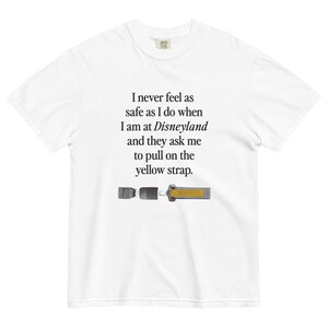 Puede incluir: Camiseta blanca con un gráfico de texto negro que dice "Nunca me siento tan seguro como cuando estoy en Disneyland y me piden que tire de la correa amarilla." El gráfico también incluye una pequeña imagen de una correa amarilla.