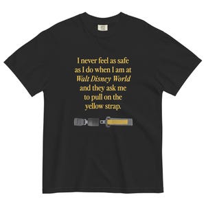 Könnte beinhalten: Schwarzes T-Shirt mit einer goldenen Grafik eines Sicherheitsgurts und dem Text "Ich fühle mich nie so sicher wie in Walt Disney World, wenn sie mich bitten, am gelben Gurt zu ziehen."