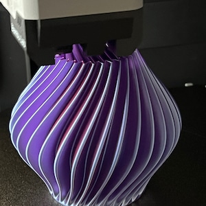 May include: A 3D printed vase with a swirling, pleated design in shades of purple and white.