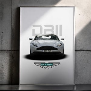 May include: Framed print featuring a white Aston Martin DB11 sports car. The car is centered, with the DB11 model name above and the Aston Martin logo below. The background is a gradient of white to black.