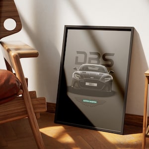 May include: A black and white poster with a black Aston Martin DBS Superleggera car in the center. The car has a black license plate that reads "DBS1". The text "DBS" is in large white letters above the car. The text "ASTON MARTIN" is in white letters below the car. The poster has a black background and a white Aston Martin logo in the bottom center.