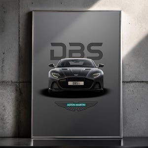 May include: Framed poster featuring a black Aston Martin DBS sports car. The car is centered against a gray background with the word "DBS" above it. The Aston Martin logo is at the bottom, with the text "Aston Martin".
