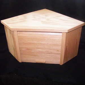 May include: A light wood corner cabinet with a hinged door and a small handle. The cabinet is made of solid wood and has a natural finish.