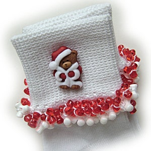 May include: White knitted cuff with a red and white beaded trim. A brown teddy bear button wearing a Santa hat and coat is attached to the cuff. The cuff is folded over, showing the texture of the knit.