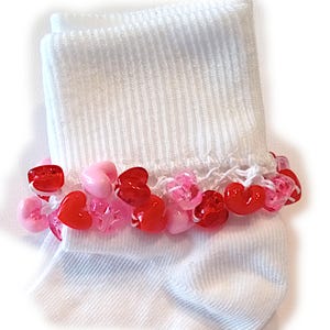 May include: White ankle socks with a crocheted trim decorated with pink and red heart-shaped beads.