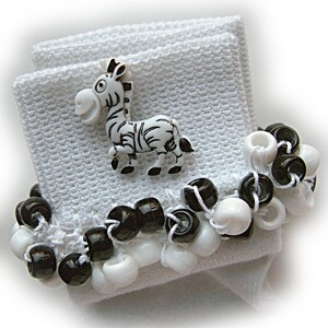 May include: A white fabric wristband featuring a cartoon zebra button in black and white. The wristband is decorated with a row of alternating black and white plastic beads strung on white thread, creating a high-contrast monochrome accessory.