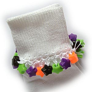May include: A white knit sock featuring a decorative cuff adorned with a row of colorful star-shaped plastic beads. The beads are arranged in a repeating pattern of black, lime green, purple, and bright orange, attached with white thread.