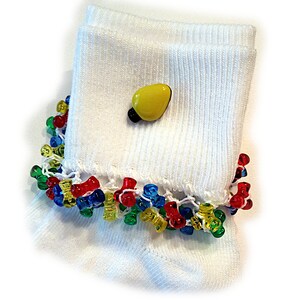 May include: A white ribbed ankle sock featuring a decorative yellow light bulb charm attached to the cuff. The hem of the sock is adorned with a row of translucent, multi-colored plastic beads in shades of red, blue, green, and yellow.