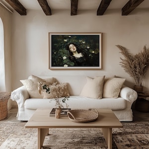 May include: A framed painting of a woman in a dark dress amongst lily pads, displayed above a white sofa with beige cushions. A wooden coffee table with a woven basket and decorative items is in front of the sofa.