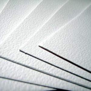 May include: Close-up of several sheets of white textured paper, fanned out. Three dark pencils are visible, with their tips pointing towards the upper right corner. The paper has a subtle, grainy texture.