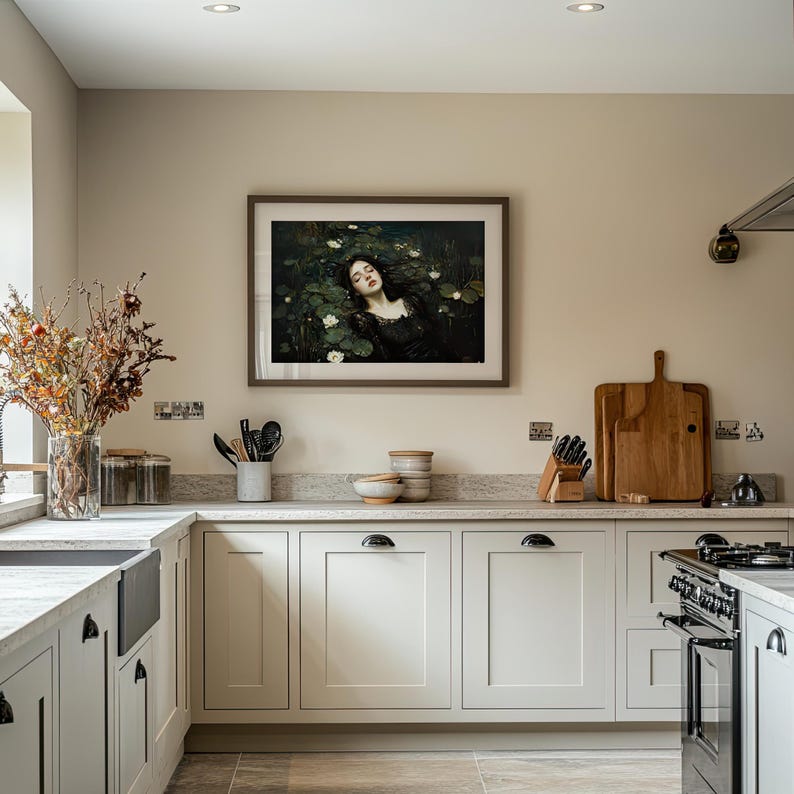 May include: A kitchen featuring light grey cabinets, a marble worktop, and a black farmhouse sink. A framed painting adorns the wall above the work surface. A vase of dried flowers sits on the counter. A black stove is visible.