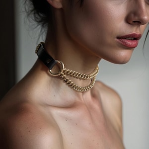 Può includere: Un girocollo a catena dorata con un cinturino in pelle nera e un anello argentato.