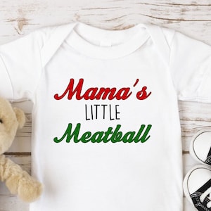 May include: White baby onesie with red and green text that reads "Mama's Little Meatball".