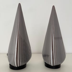 Könnte beinhalten: Zwei kegelförmige Tischlampen mit einem schwarz-weißen Streifenmuster. Die Lampen haben einen schwarzen Sockel und eine spitze Spitze. Die Lampen stehen auf einer weißen Oberfläche.