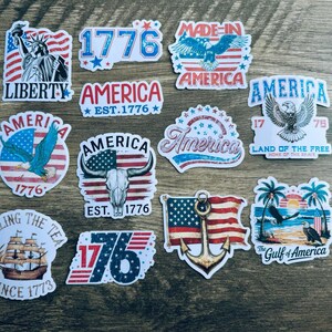 May include: A collection of patriotic stickers featuring American flags, eagles, and the Statue of Liberty. Designs include the text "Liberty," "America," "1776," and "Land of the Free." The stickers are in red, white, and blue.