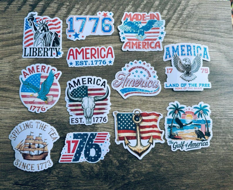 May include: A collection of patriotic stickers featuring American flags, eagles, and the Statue of Liberty. Designs include the text "Liberty," "America," "1776," and "Land of the Free." The stickers are in red, white, and blue.