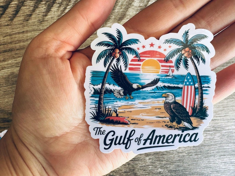 May include: A sticker featuring a coastal scene with palm trees, an eagle in flight, and another perched on the beach. A surfboard with a red, white, and blue design is also present. The text "The Gulf of America" is displayed.