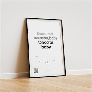 Peut inclure: Une affiche encadrée avec le texte "Donne-moi ton coeur, baby ton corps baby" en gris. L'affiche a un cadre noir et est appuyée contre un mur blanc sur un sol en bois. Un code QR et le mot "Variante" sont en bas.
