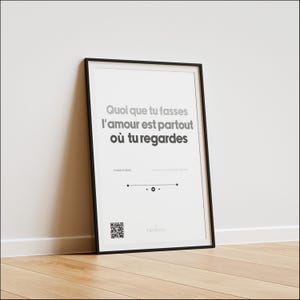 Puede incluir: Impresión artística enmarcada con la cita francesa "Quoi que tu fasses l'amour est partout où tu regardes" en texto gris y negro. La impresión está en un marco negro y se apoya en una pared blanca sobre un suelo de madera.