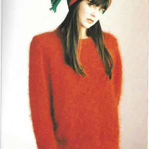 May include: A woman wearing a red fuzzy sweater with a green and red turban. She is wearing a green skirt.