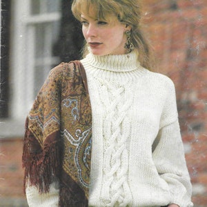 May include: A white cable knit sweater with a high turtleneck and a brown and gold paisley scarf.