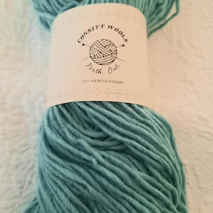 Può includere: Primo piano di un gomitolo di lana color turchese. L'etichetta recita "CONSITT WOOLS Perth, Ont. Span and Milled in Canada". La lana appare morbida e spessa, adatta per progetti di maglieria o uncinetto.