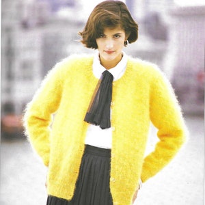 Könnte beinhalten: Ein leuchtend gelber, flauschiger Cardigan mit Knopfverschluss. Der Cardigan wird über einem weißen Hemd mit Kragen und einem schwarzen Faltenrock getragen. Ein schwarzer Schal ist am Hals gebunden.