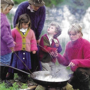 Puede incluir: Un grupo de personas, incluidos niños, se encuentran alrededor de una olla grande sobre un fuego. Llevan suéteres de punto de colores. La olla está humeante y sale humo del fuego.