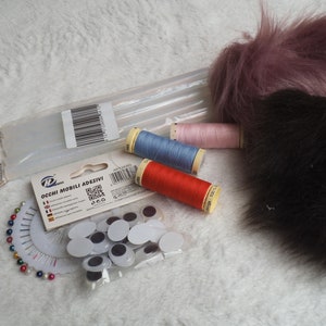 May include: A set of craft supplies for making plush toys, including two different colors of faux fur, four spools of thread in red, blue, pink, and white, a package of googly eyes, and a package of sewing pins.
