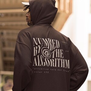 Puede incluir: Una sudadera con capucha marrón con el texto "Numbered by the Algorithm" impreso en la espalda. El texto está en una fuente blanca estilizada con un diseño circular. El texto también incluye las palabras "infinite feed" y "attention span not found error 152".