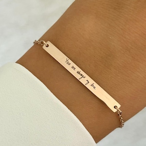 Può includere: Un braccialetto a barra in oro rosa con una catena delicata. La barra ha l'iscrizione "You are always my love" scritta in corsivo.