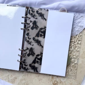 May include: Open planner with white pages and a patterned divider. The divider has a black and white animal print design. The planner is open on a light-colored surface.