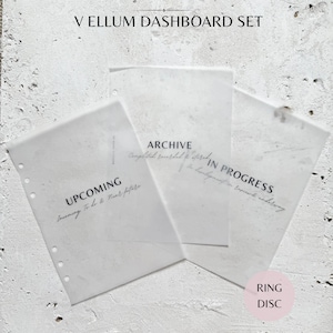 May include: A set of three translucent vellum dashboard sheets for a planner, featuring the printed text V ELLUM DASHBOARD SET, UPCOMING, ARCHIVE, and IN PROGRESS, with punched holes along the left side for ring binding and a pink circular label.