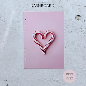 May include: A light pink planner dashboard featuring a heart shape formed by two red and white striped candy canes in the center. The rectangular sheet has six circular punch holes along the left edge and the word DASHBOARD printed at the top.