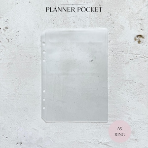 May include: A clear, transparent planner pocket with a top flap and pre-punched holes for ring binders. The text "PLANNER POCKET" is at the top, and "A5 RING" is in a pink circle at the bottom. The pocket is designed for A5 size paper.