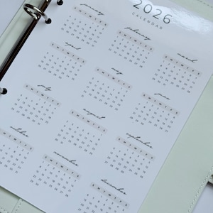 Pode incluir: Um inserto de calendário de 2026 para uma pasta, com layouts mensais e datas em uma fonte minimalista. O calendário é impresso em papel branco e foi projetado para ser inserido em uma pasta de argolas. O calendário inclui os meses de janeiro a dezembro.