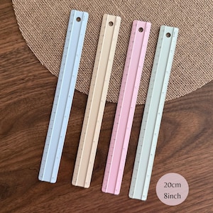 May include: Four straight rulers in light blue, beige, pink, and pale green, each featuring a circular hole at the top. The rulers display markings for 20 cm and 8 inches, with clear numerical increments printed along the side of each tool.