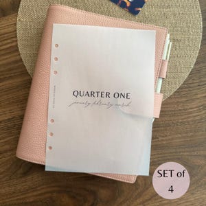 May include: A light pink leather planner with a translucent vellum dashboard insert. The insert features the black text QUARTER ONE, january february march, and the brand name Marcella Paper Co. A circular sticker reads SET of 4.