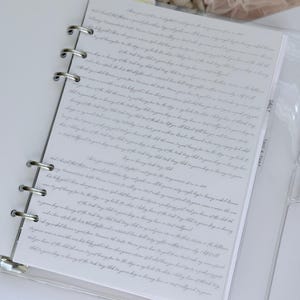 Puede incluir: Un archivador transparente de tres anillas con papel rayado y un separador de plástico con la etiqueta "Daily & That". El papel está lleno de texto manuscrito en tinta gris claro. Una pequeña tarjeta con el texto "Life is Better in A Tutu" es visible en el fondo.