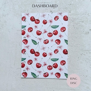 Könnte beinhalten: Ein rechteckiges Planer-Dashboard mit weißem Hintergrund und einem sich wiederholenden Muster aus roten Kirschen, grünen Blättern und kleinen rosa Blüten. Die linke Kante hat sechs runde Stanzlöcher. Der Text DASHBOARD steht oben.