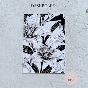 May include: A rectangular planner dashboard featuring a black and white botanical illustration of lily flowers and leaves. The paper has six circular punch holes along the left edge for ring binding. The text DASHBOARD is printed at the top center.