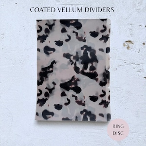 Puede incluir: Separadores de vitela recubiertos con un patrón moteado en tonos negros, marrones y grises. Los separadores tienen forma rectangular con esquinas redondeadas. El texto "COATED VELLUM DIVIDERS" está en la parte superior y "RING DISC" en un círculo rosa en la parte inferior.