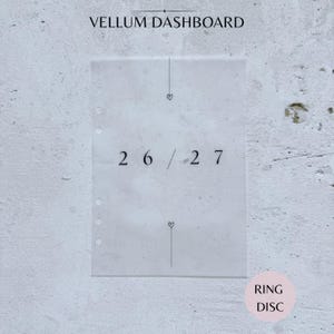May include: A translucent vellum dashboard for a planner featuring the text VELLUM DASHBOARD at the top and 26 / 27 in the centre. The sheet has a vertical line with a small heart icon above and below the numbers and six punched holes on the left side.