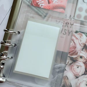 May include: A clear, plastic binder with silver metal rings, holding various inserts. One insert contains a white sticky note. Other inserts display photos of pink sneakers, flowers, and text that reads "VERY ISY 2013".