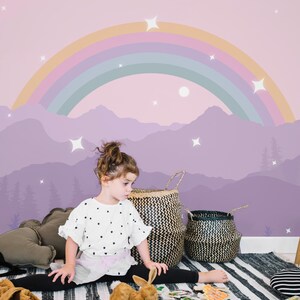Pu&ograve; includere: Una cameretta con un murale raffigurante un arcobaleno, montagne e stelle nei toni del viola e del rosa. La stanza comprende cesti intrecciati, uno sgabello in legno e un tappeto a righe bianche e nere.