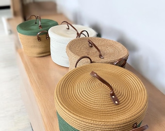 Puede incluir: Cuatro cestas redondas de almacenamiento con tapas, cada una con una combinación de colores diferente. Las cestas están hechas de material tejido y tienen asas de cuero. Las combinaciones de colores incluyen verde y beige, blanco, beige y una combinación verde y beige.