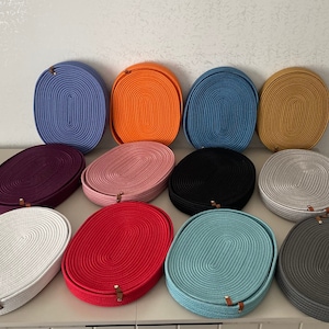 May include: A collection of 12 oval-shaped woven baskets in various colours, including white, red, pink, purple, grey, blue, and orange. The baskets are made of a rope-like material and have a unique, textured design.