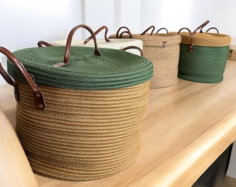 Puede incluir: Una colección de cestas redondas de almacenamiento con tapas y asas de cuero. Las cestas están hechas de material tejido en varios colores, incluyendo verde, marrón y crema. Las tapas son de un color que contrasta con el cuerpo de la cesta.