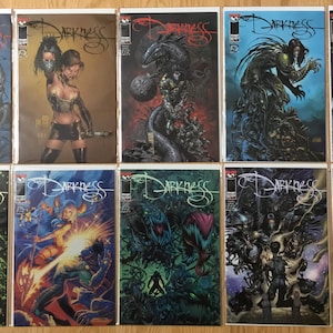 May include: A collection of twelve comic books titled "The Darkness". The covers feature various illustrations with dark, gothic themes, including figures, monsters, and abstract designs. The comic book covers are in good condition and are displayed on a wooden surface.